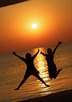 Two girls jumped on the background of the dawn sun. Focus on models. Shallow depth of field. Toned image.