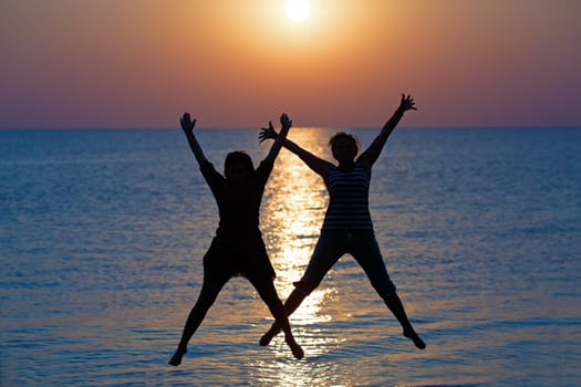 Two girls jumped on the background of the dawn sun. Focus on models. Shallow depth of field.