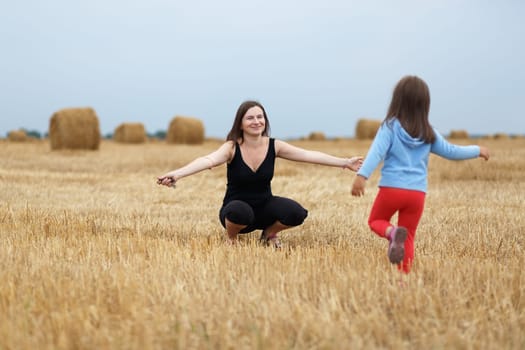Happy family. Joyful mom and her little daughter on a field of hay and straw bales. Shallow depth of field. Selective focus on mother.