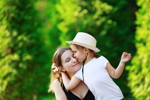 Daughter hugging her mother on the background of bright juicy green foliage. Happy family. Mom and child girl. Space for text. Shallow depth of field. Selective focus.