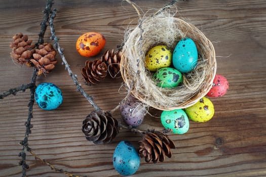 Bright Easter eggs on wooden background background. Colorful Easter still life with eggs in the nest and pine cones. Easter