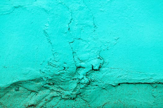 Fragment of the old wall, painted bright turquoise paint, cracked over time.