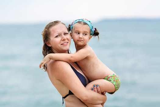 Mother and daughter at the hands of a blurred background of the sea. Focus on the models.