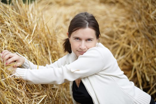 Pretty young woman in a white blouse posing on a straw background.