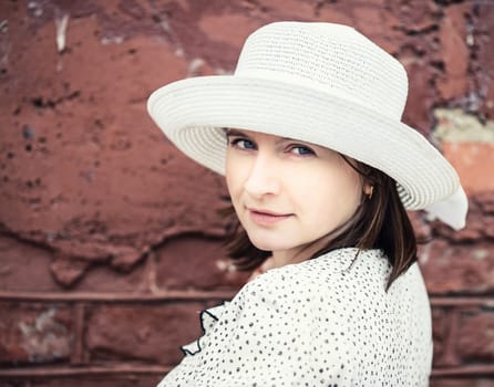 Pretty young woman in white hat against brick wall background. Close-up female portrait. Close-up vintage portrait of a woman. Selective focus. Vintage style photo.