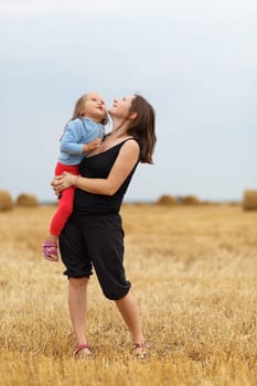 Mother and baby daughter in his arms in the straw field. Shallow depth of field. Selective focus.
