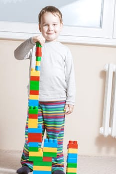 standing and smiling boy with built stack of colored cubes