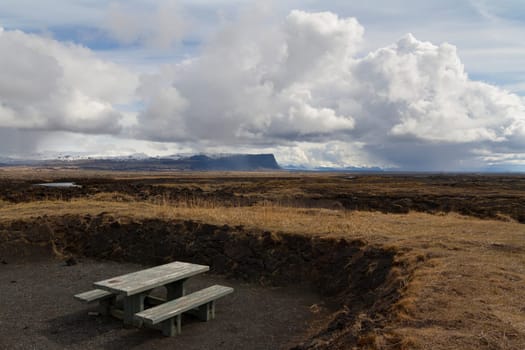 Horizontal panorama of a wooden resting bench with mountains covered in snow and dramatic clouds above