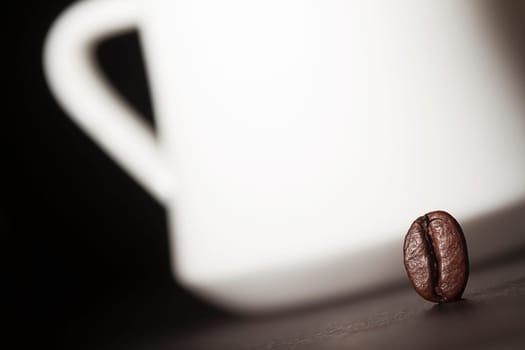Macro shot of a coffee bean with a white coffee cup silhouette in the background