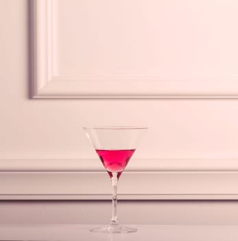 Lonely cocktail glass with pink liquid against an elegant wall.