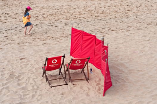 DURBAN, SOUTH AFRICA - JULY 09, 2016: Young girl walks past two Vodacom beach chairs on the beach in Umhlanga Rocks