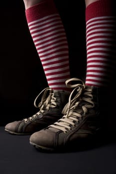 Woman’s legs with sneakers and a pair of red socks with white stripes on dark background