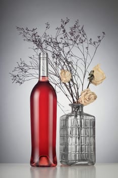Rose wine bottle with no label next to withered white roses in a vase