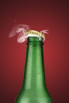 Green cold beer bottle with water drops and golden cap open on red background
