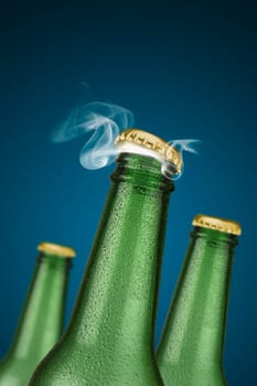 Green cold beer bottles with water drops and golden cap open on blue background