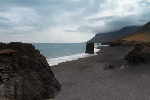 Horizontal view of an Icelandic beach with a huge rock formation in the middle