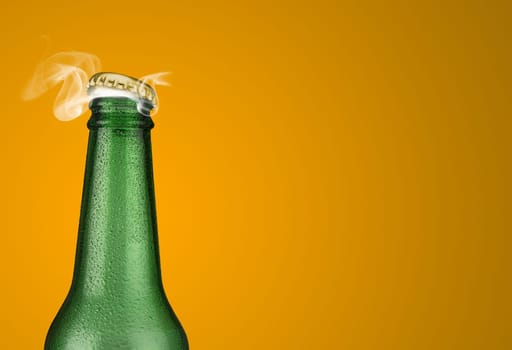 Horizontal photo of a green cold beer bottle with water drops and golden cap open on yellow background