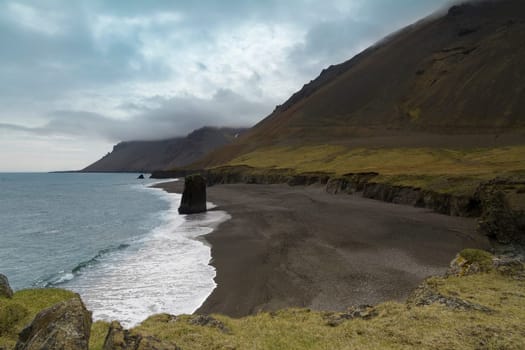 Horizontal view of an Icelandic beach with a huge rock formation in the middle