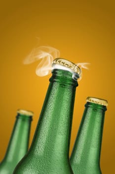 Green cold beer bottle with water drops and golden cap open on yellow background