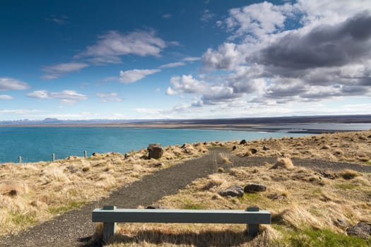 Horizontal panorama of a wooden resting bench with a beautiful shoreline in the background and dramatic clouds above