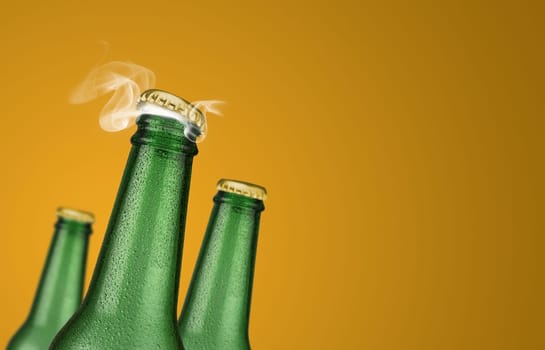 Horizontal photo of three green cold beer bottles with water drops and golden cap open on yellow background