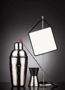 Cocktail set of tools including shaker and spoon next to a table stander with display area for offers or headline