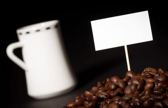A pile of coffee beans with an empty sign on top of them and a white coffee cup in the background