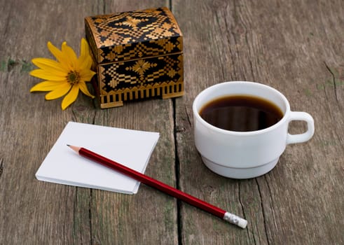 casket, coffee, pencil with paper and a yellow flower, a still life a subject drinks