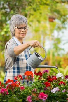 Beautiful mature woman in a garden watering flowers