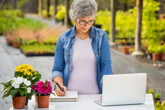 Beautiful mature woman working in a greenhouse holding flowers on her hands