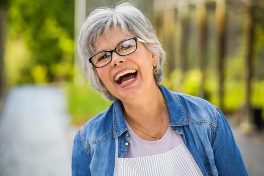 Beautiful mature woman working in a greenhouse, looking at camera while laughing