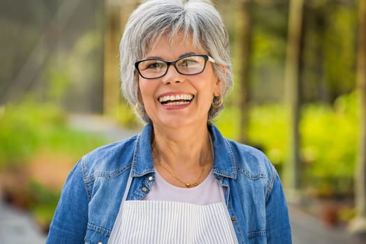 Beautiful mature woman working in a greenhouse, looking at camera while laughing