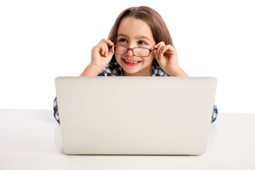 Little girl sitting on a desk and working with a laptop