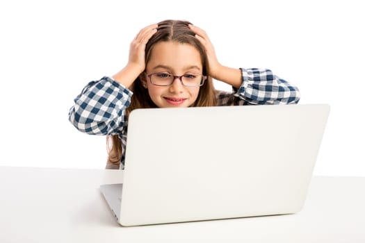 Little girl sitting on a desk and working with a laptop