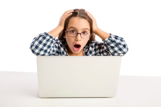 Little girl sitting on a desk and working with a laptop