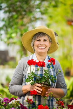 Beautiful mature woman working in a greenhouse holding flowers on her hands