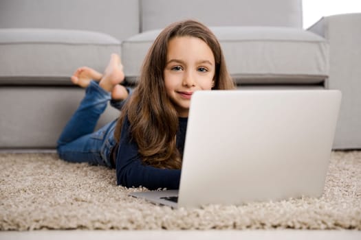 Happy little girl at home working with a laptop