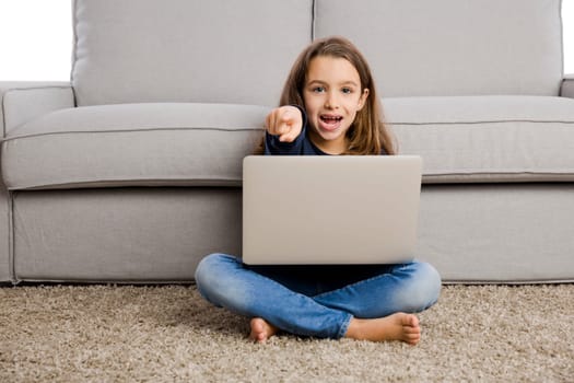Happy little girl at home working with a laptop