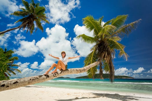 Beautiful woman sitting on a palmtree in La Digue, Seychelles
