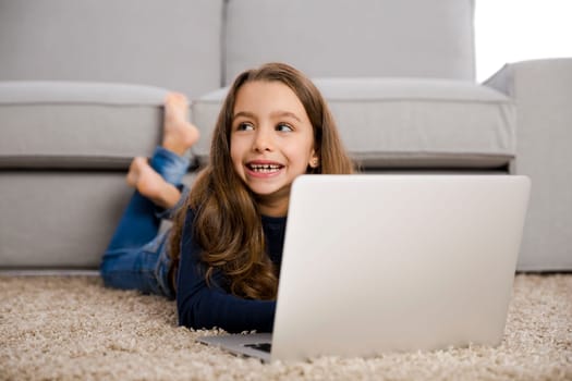 Happy little girl at home working with a laptop