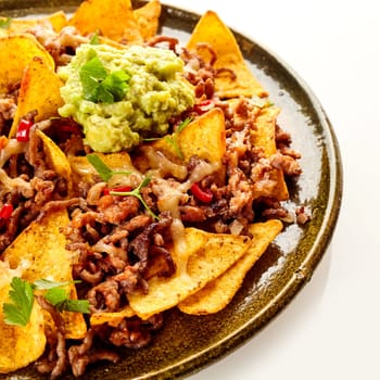 Close up cropped view on round ceramic plate of yellow corn tortilla chips, cheese and beef garnished with cilantro and red peppers