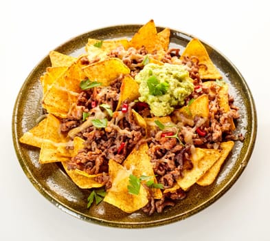 Top down view on circular ceramic plate with chips, cheese and ground beef over white background with soft set down shadow