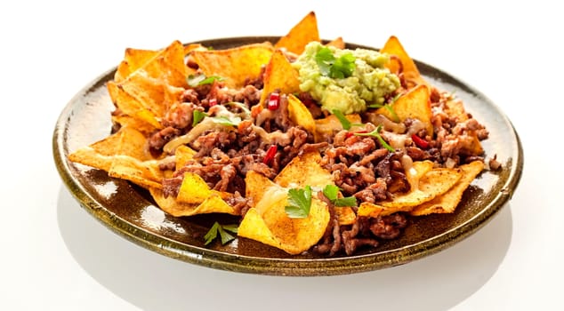 Round ceramic plate with crunchy yellow corn tortilla chips, cheese and beef over white background with soft set down shadow