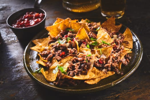 Tortilla chips garnished with ground beef, melted cheese, peppers and cilantro leaves in plate on wooden table