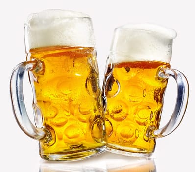Two glass beer mugs full of golden lager with thick frothy heads over a reflective white background conceptual of the Oktoberfest