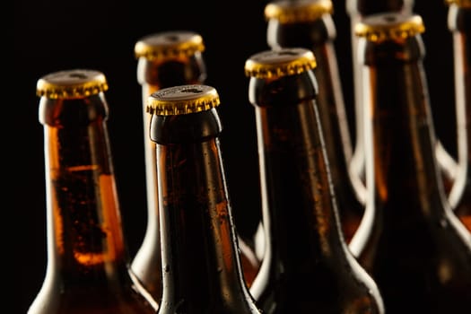 Rows of sealed beer bottles in a close up view of the necks and tops with selective focus to one in the foreground over a black background