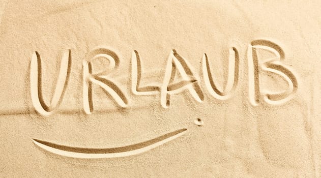 The word Urlaub, or Holiday, written in golden beach sand conceptual of annual summer vacations in the tropics at a beach front resort in a wide angle banner format