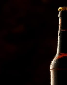 Cold frosted beer bottle border with a partial view of a sealed full bottle of lager or beer over a black background with copy space