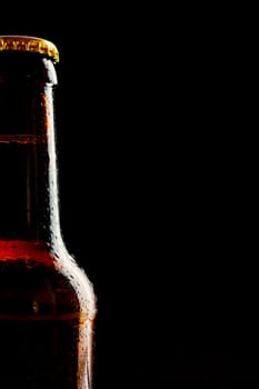Single partial unlabelled ice cold beer bottle as a border over a black background with copy space for Oktoberfest