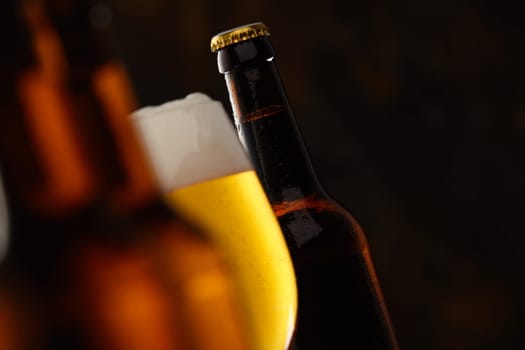 Glass of glowing golden frothy beer in a selective focus view between to beer bottles with copy space for Oktoberfest, tilted angle perspective